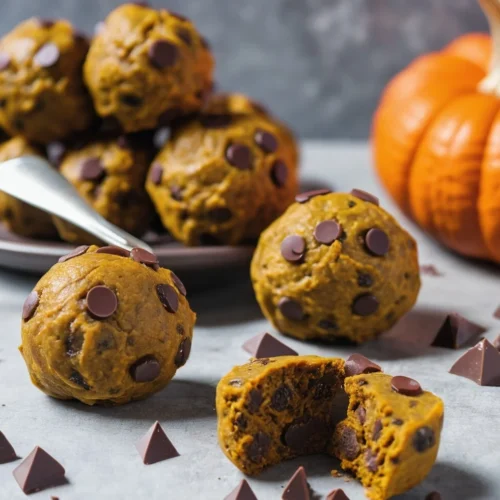 Pumpkin protein balls with chocolate chips on a plate, surrounded by scattered chocolate chunks and a decorative pumpkin in the background.